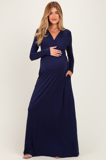 woman wearing a navy blue long sleeve maternity maxi dress and showing her baby bump with hands in pockets