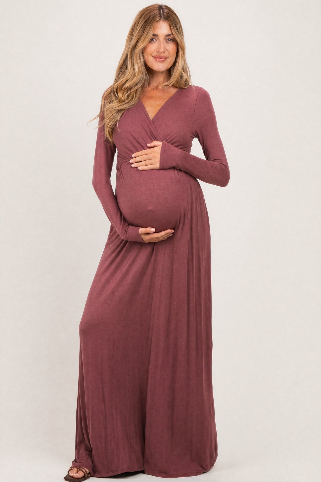 woman wearing a mauve long sleeve maternity dress and holding her baby bump