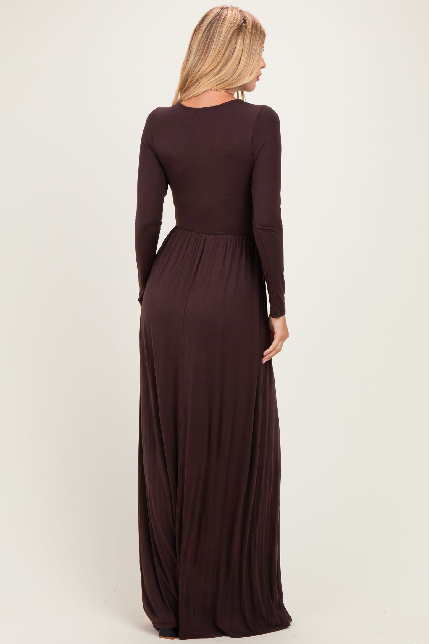 woman wearing a long sleeve brown maxi dress with a fitted bodice and flowy skirt, viewed from the back