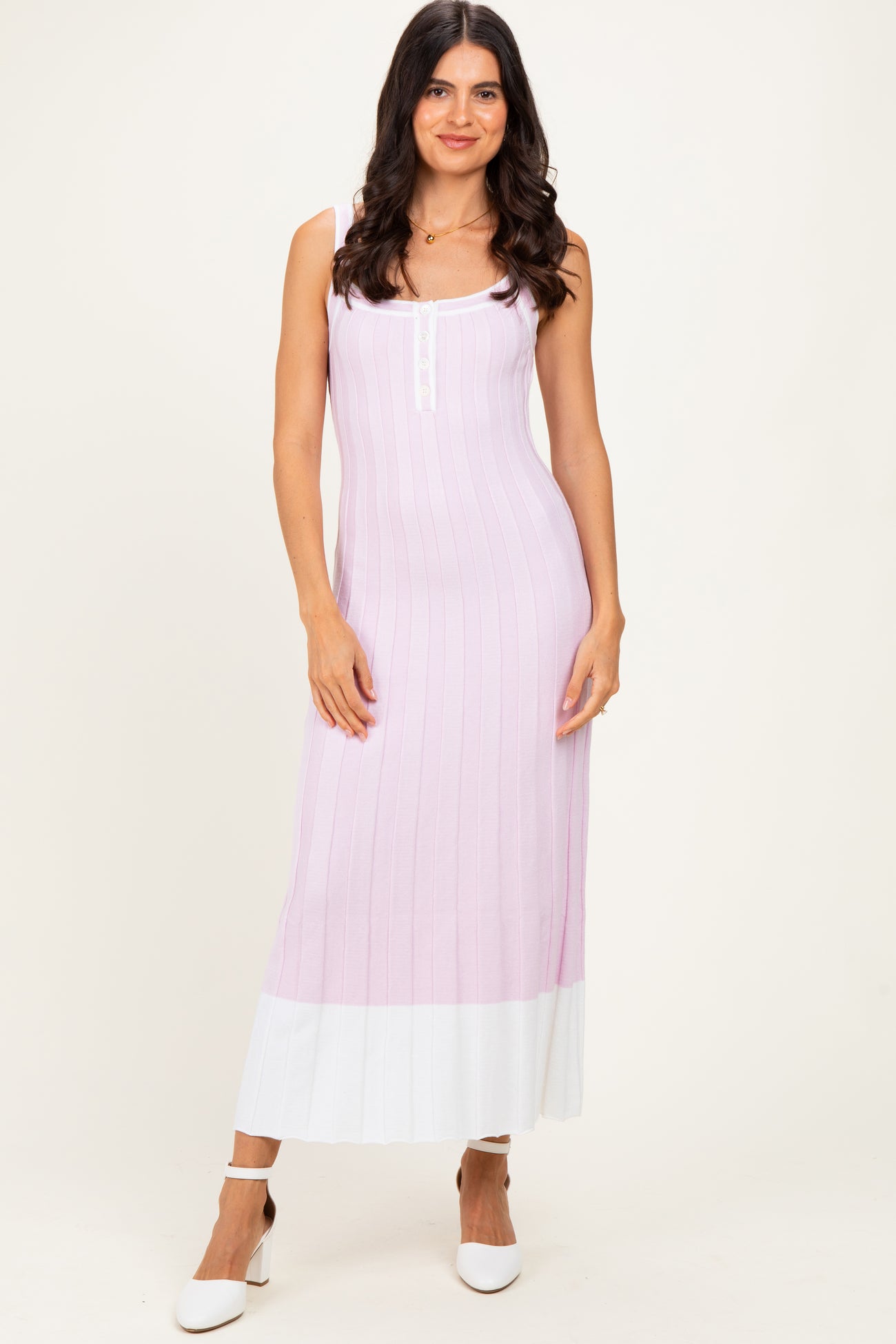 woman wearing a light pink ribbed maxi dress with white hem and decorative buttons, standing with one hand on her hip