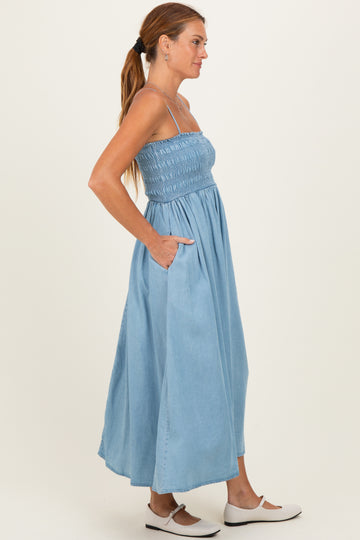 woman wearing a light blue maxi dress with smocked bodice and pockets, standing sideways with long hair tied back
