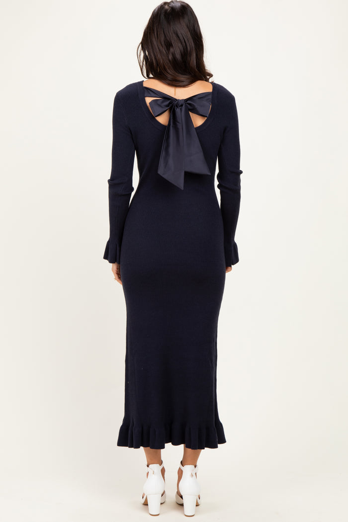 woman wearing a navy blue ribbed long sleeve dress with a back bow detail and ruffled hemline