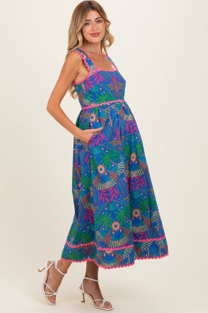 woman wearing a vibrant blue maternity dress with floral patterns and pockets, showcasing her baby bump