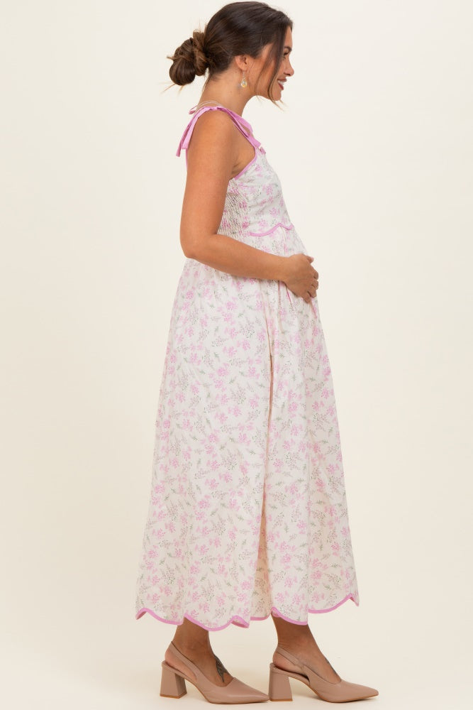 woman wearing a floral print maternity maxi dress with pink trim and holding her baby bump