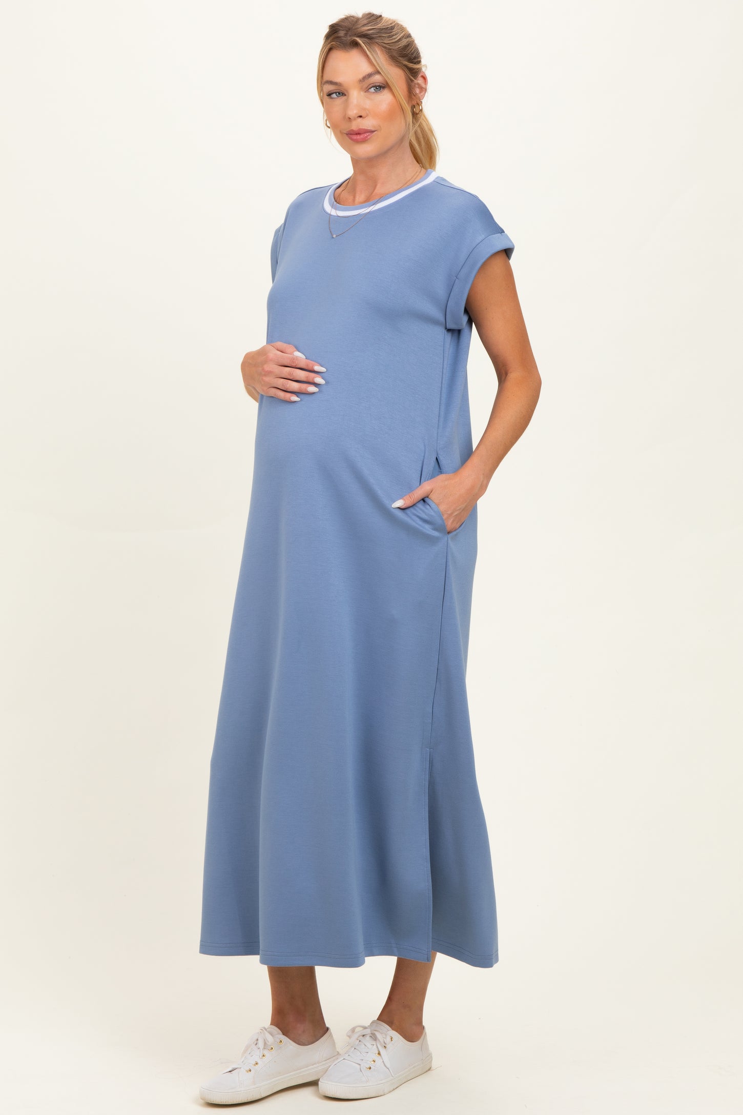 woman wearing a light blue maternity dress with short sleeves and pockets, gently cradling her baby bump