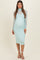 woman wearing a light mint green maternity dress with a fitted silhouette and long sheer sleeves, showing her baby bump
