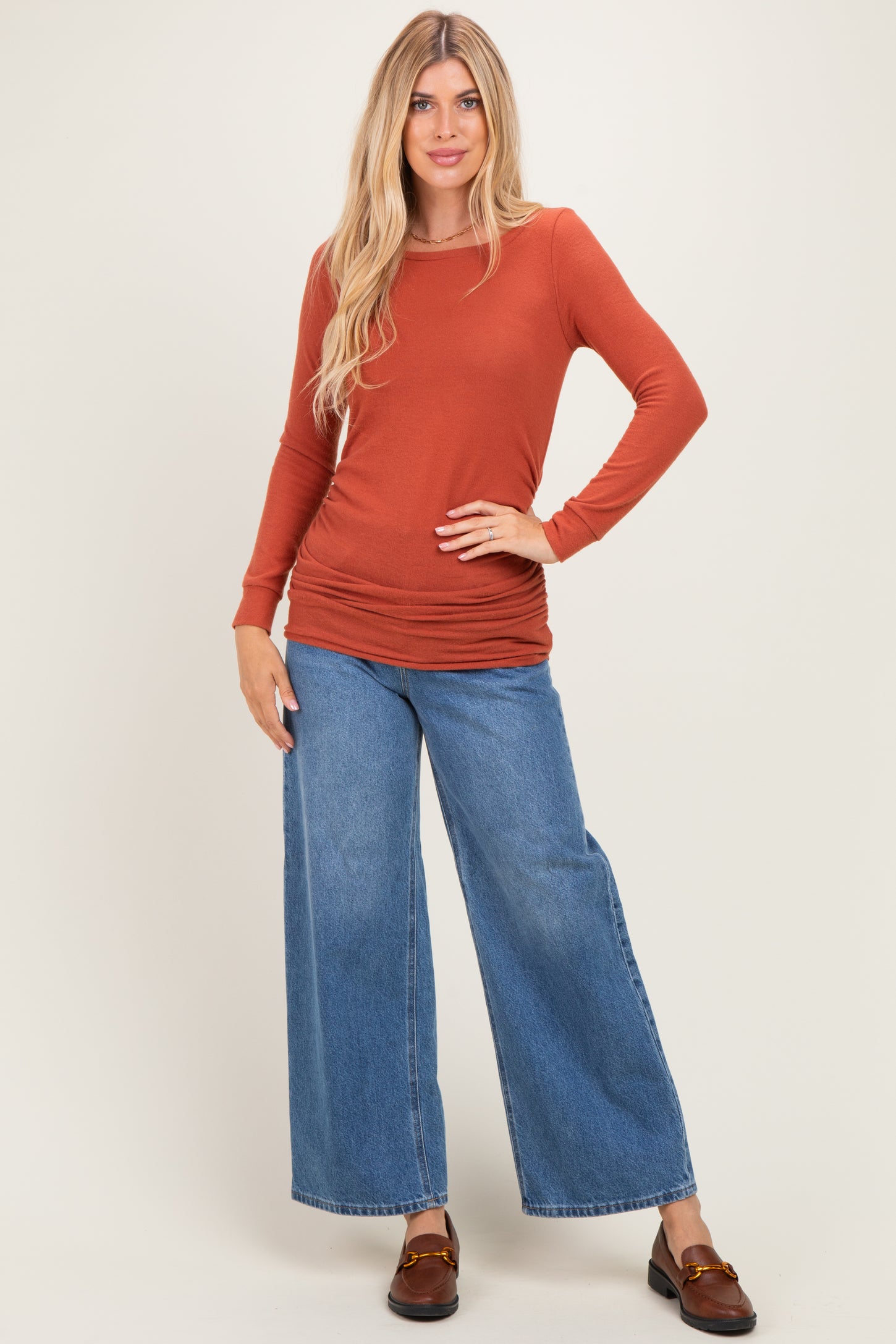 woman wearing a rust long sleeve top and wide-leg blue jeans standing with hands on hips