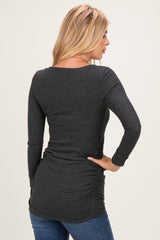 woman wearing a dark gray long sleeve top with gathered side detail, facing away from the camera