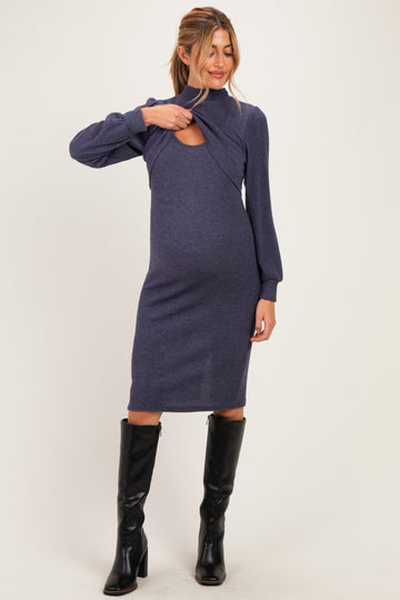woman wearing a dark blue maternity dress with cut-out detailing and long sleeves, showcasing her baby bump
