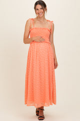 woman wearing a coral maternity maxi dress with adjustable straps, smocked bodice, and holding her baby bump