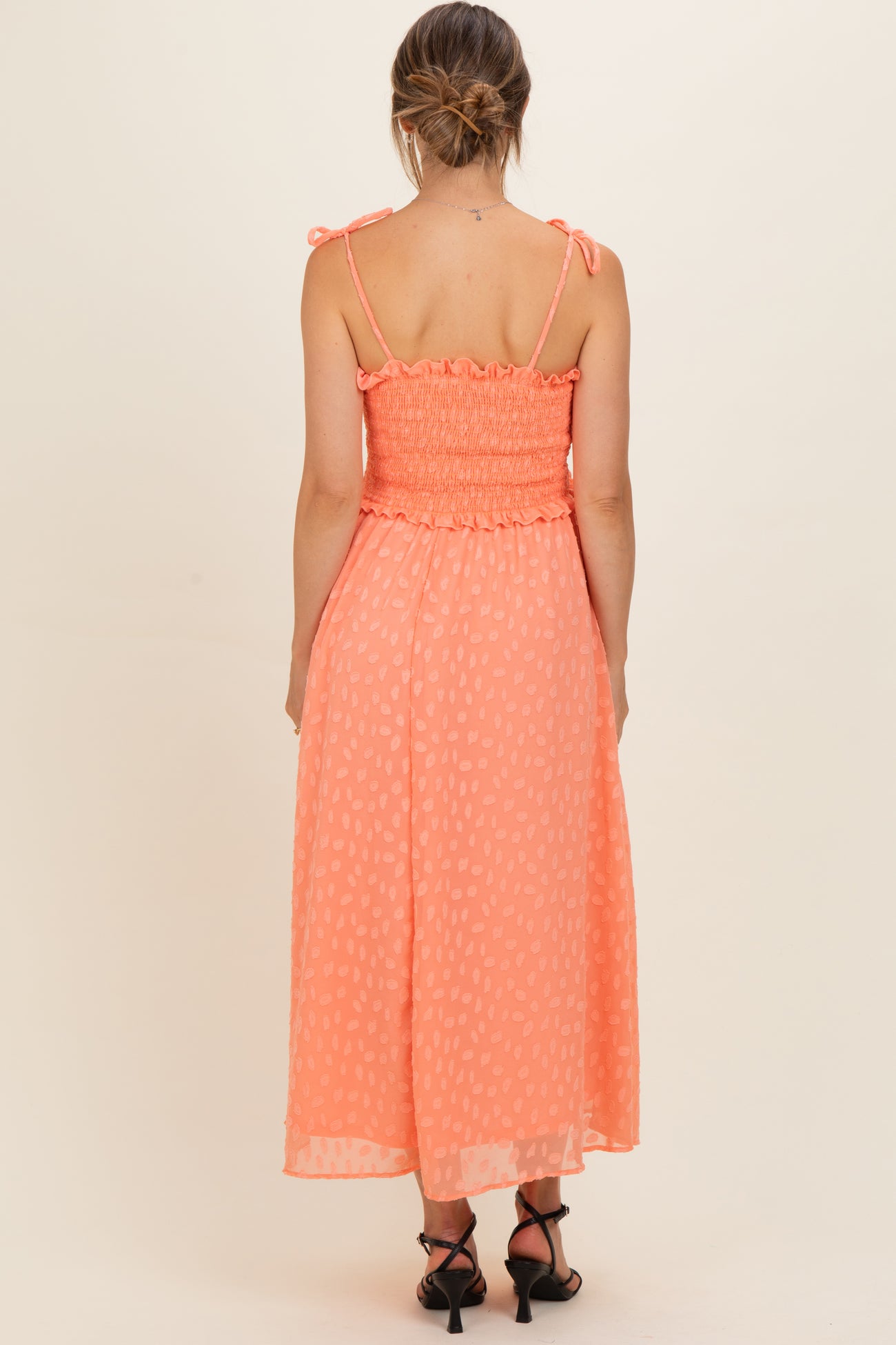 woman wearing a coral maternity dress with smocked detailing and adjustable straps, showcasing a flowing skirt