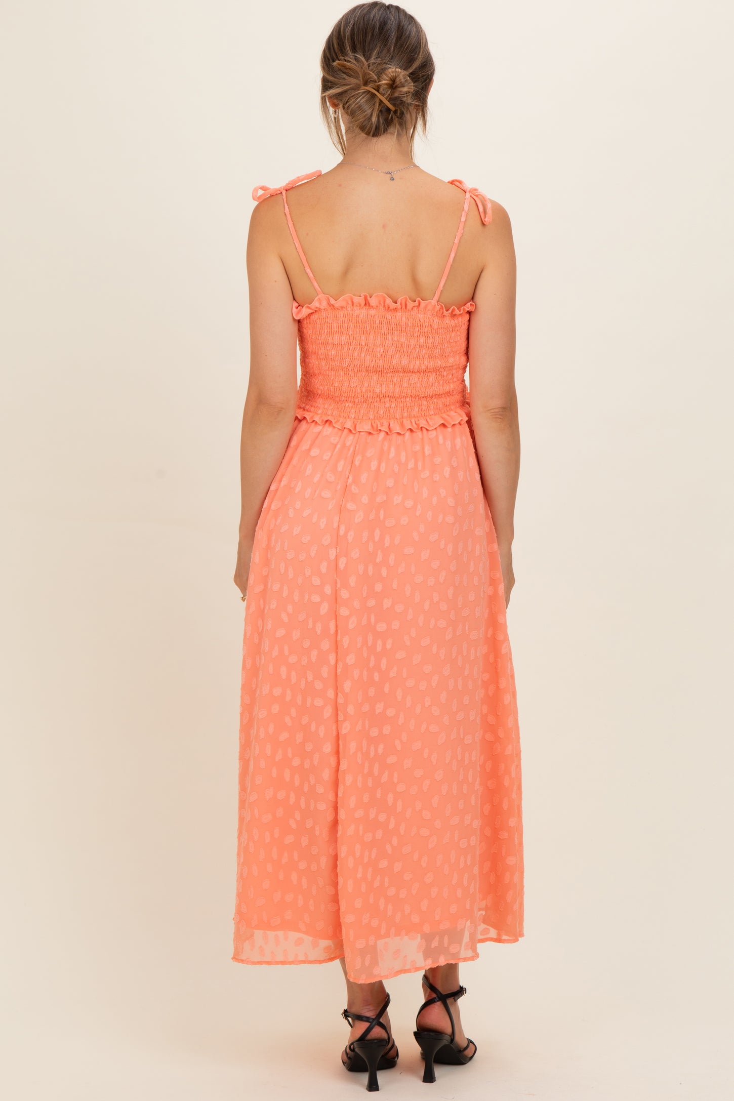 woman wearing a coral maternity dress with smocked detailing and adjustable straps, showcasing a flowing skirt