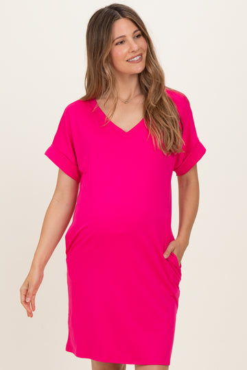 woman wearing a bright pink v-neck maternity dress with short sleeves and pockets, showcasing her baby bump