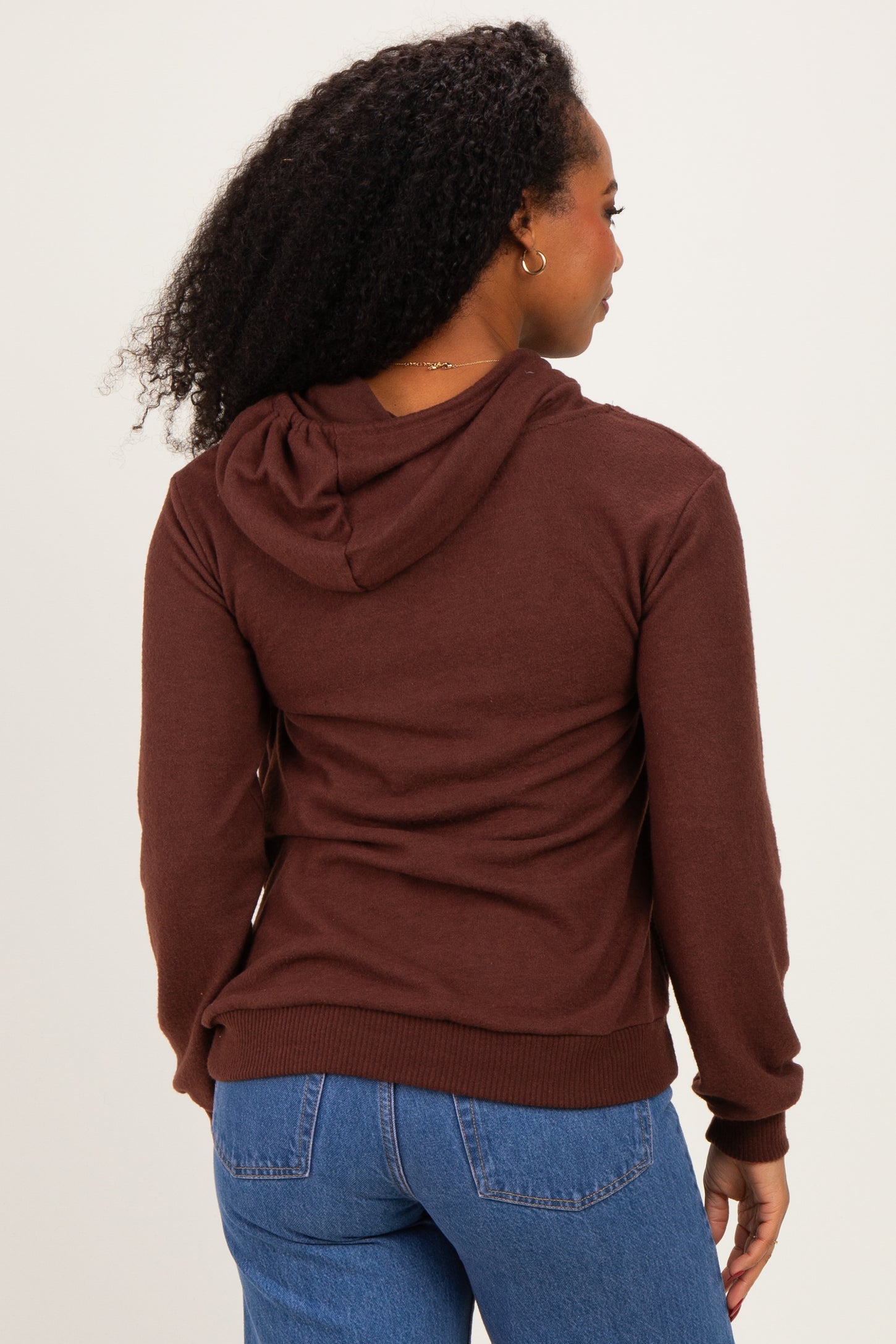 woman wearing a brown hooded sweatshirt, shown from the back, paired with blue jeans