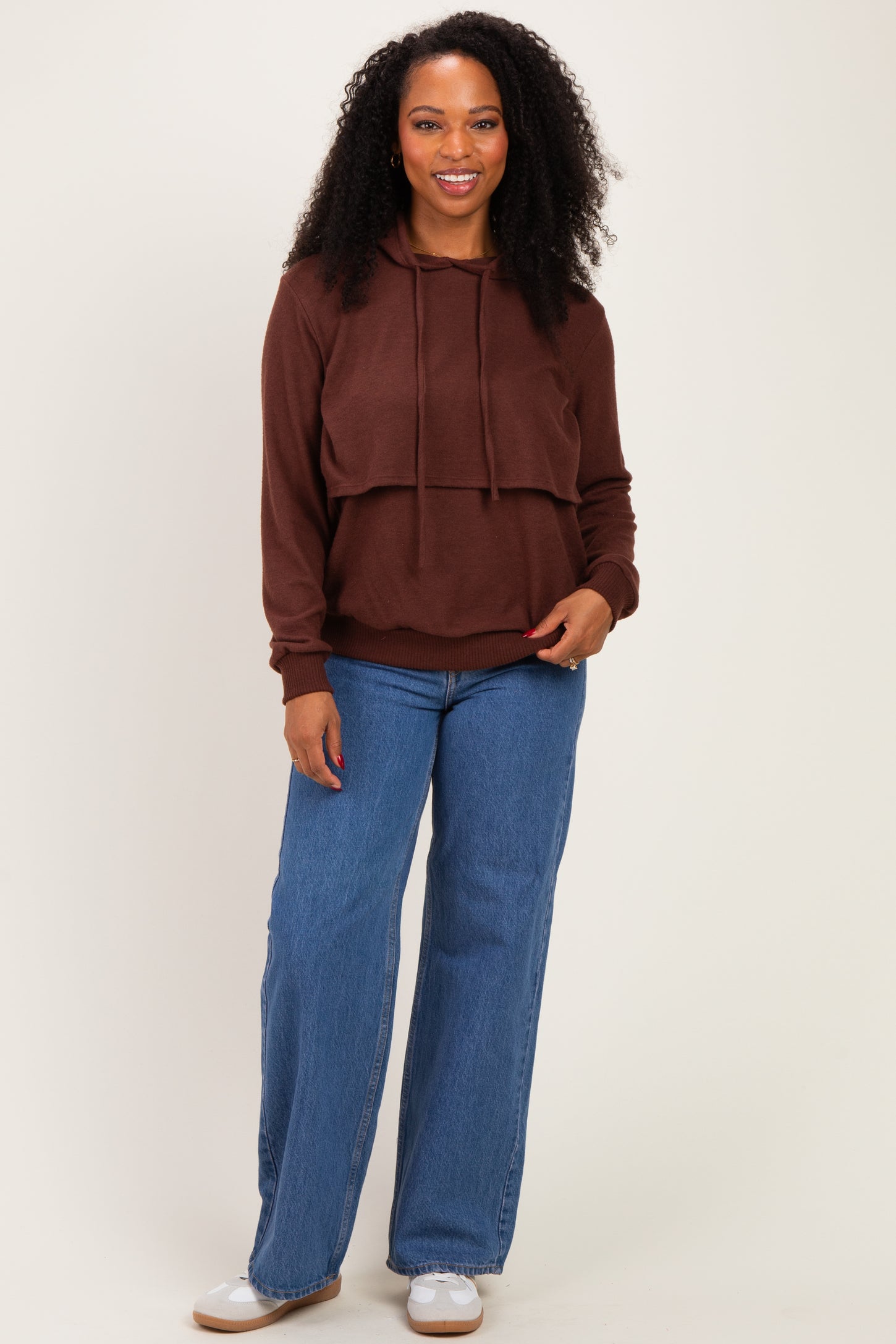 woman wearing a brown cropped hoodie with a layered look and blue wide-leg jeans