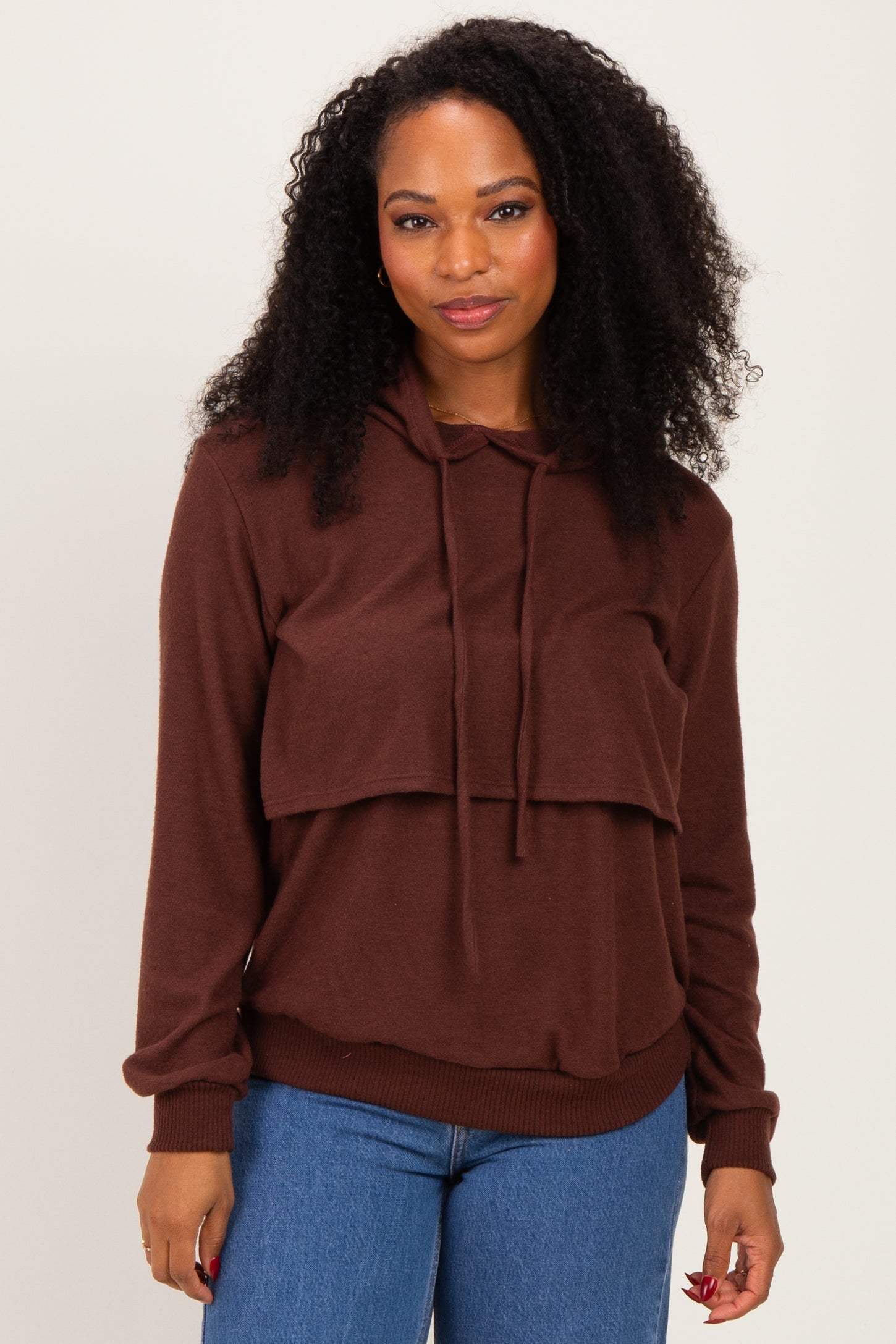 woman wearing a brown oversized hoodie with a layered design and long sleeves, paired with blue jeans