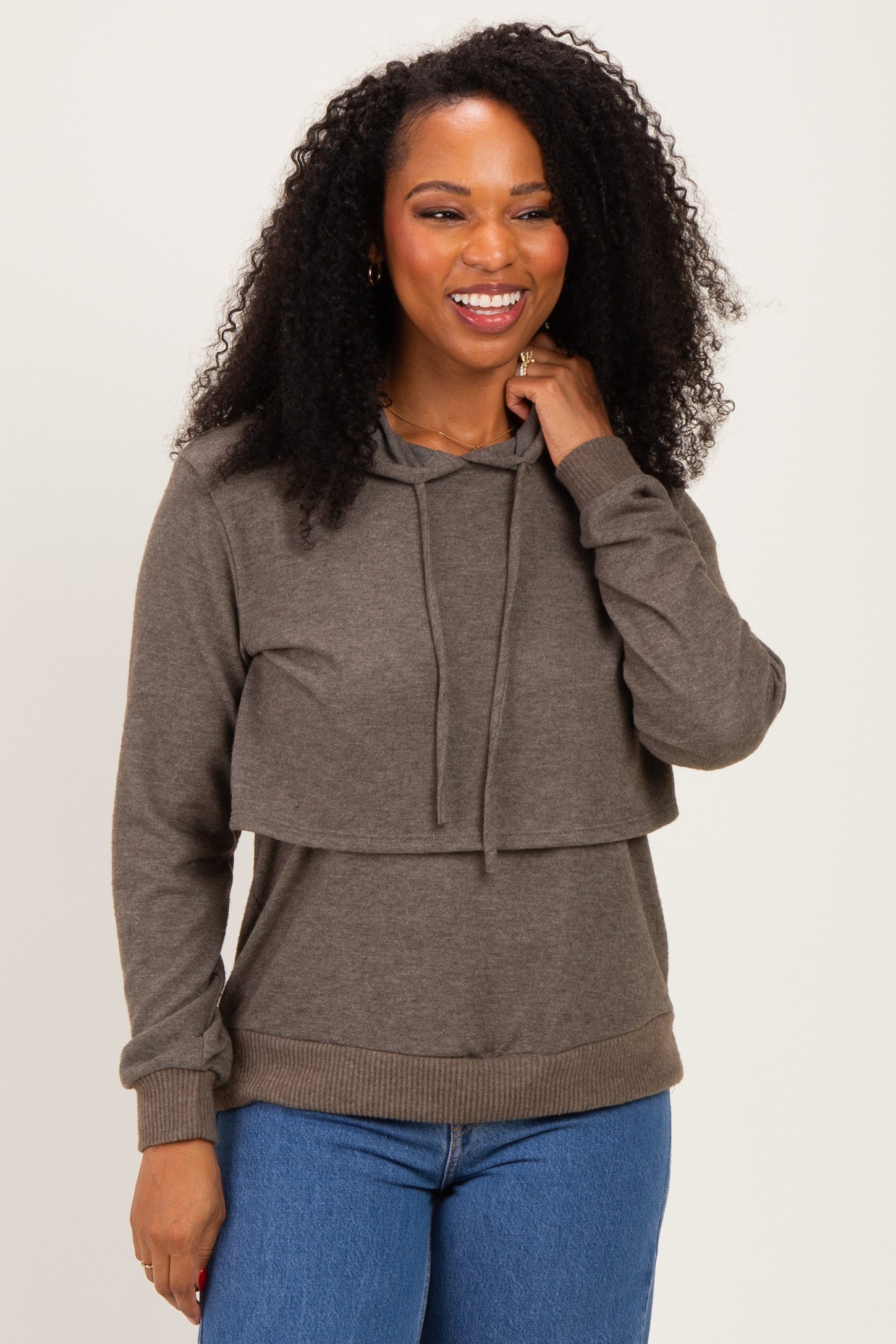 woman wearing a dark gray layered hoodie with a front flap and long sleeves paired with blue jeans