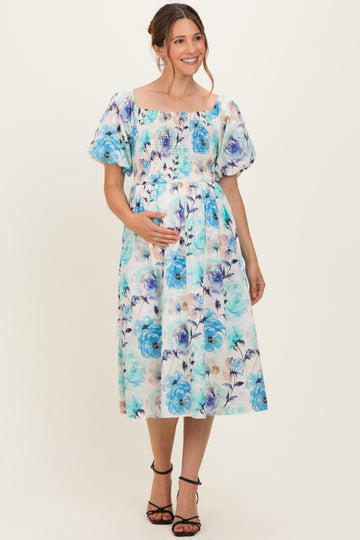 woman wearing a floral maternity dress with puff sleeves and a smocked bodice, holding her baby bump