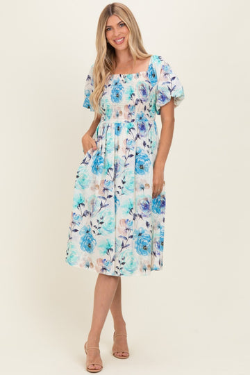 woman wearing a floral printed midi dress with puff sleeves and a smocked bodice, standing with hands in pockets