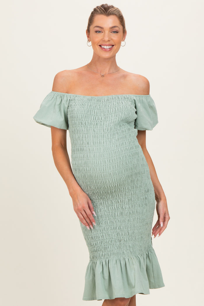 woman wearing a light green off-the-shoulder maternity dress with smocking and ruffled hem, showcasing her baby bump