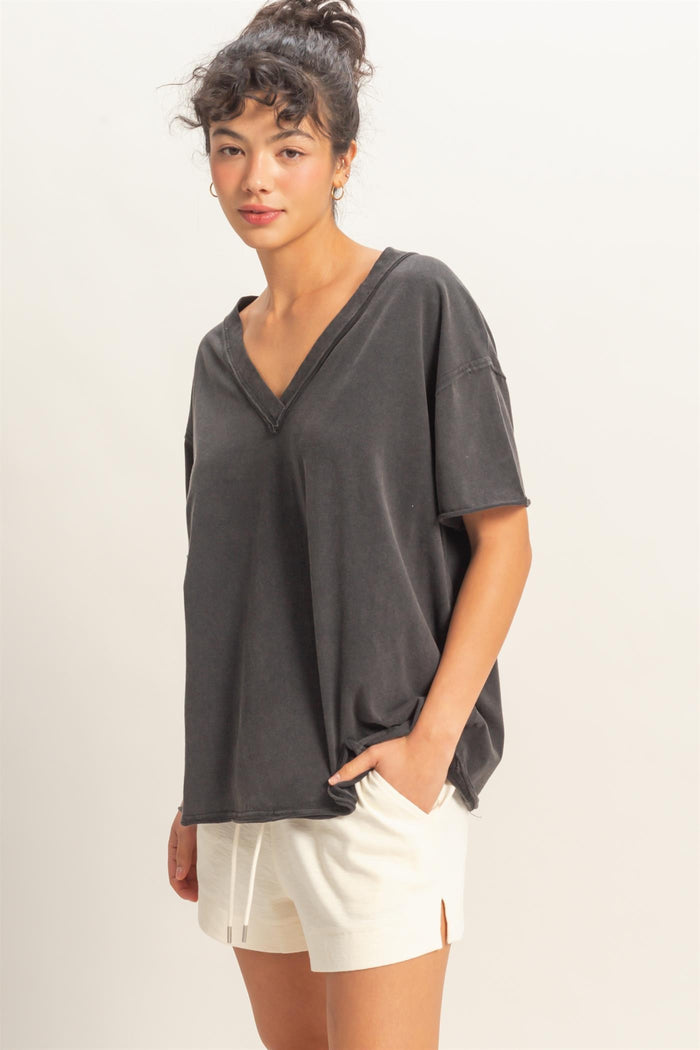woman wearing a charcoal gray oversized v-neck tee with short sleeves and cream-colored shorts