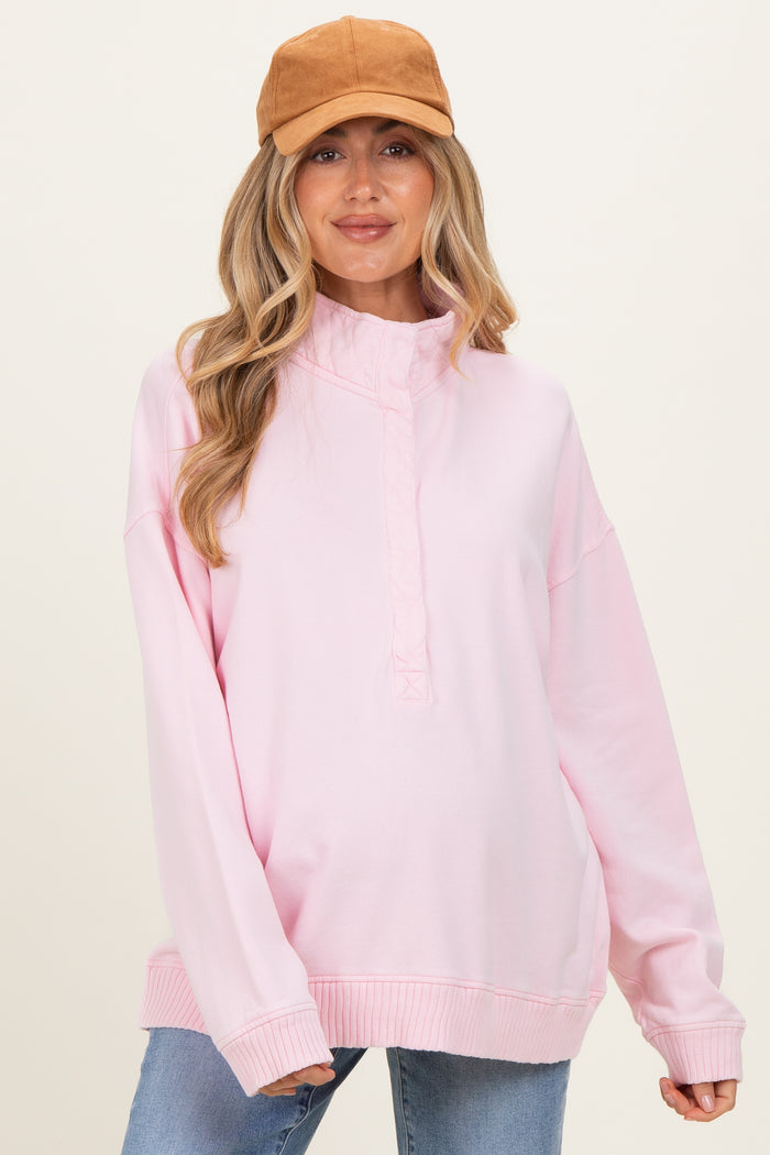 woman wearing a light pink maternity sweatshirt with a high neckline and long sleeves, styled with a tan cap