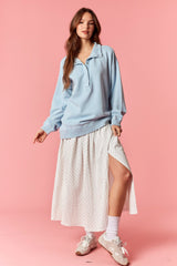 woman wearing a light blue oversized pullover and a white polka dot maxi skirt with a side slit and white sneakers