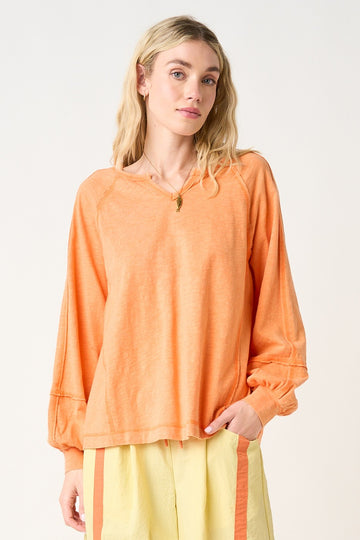 woman wearing an orange long sleeve relaxed fit top with balloon sleeves and a round neckline