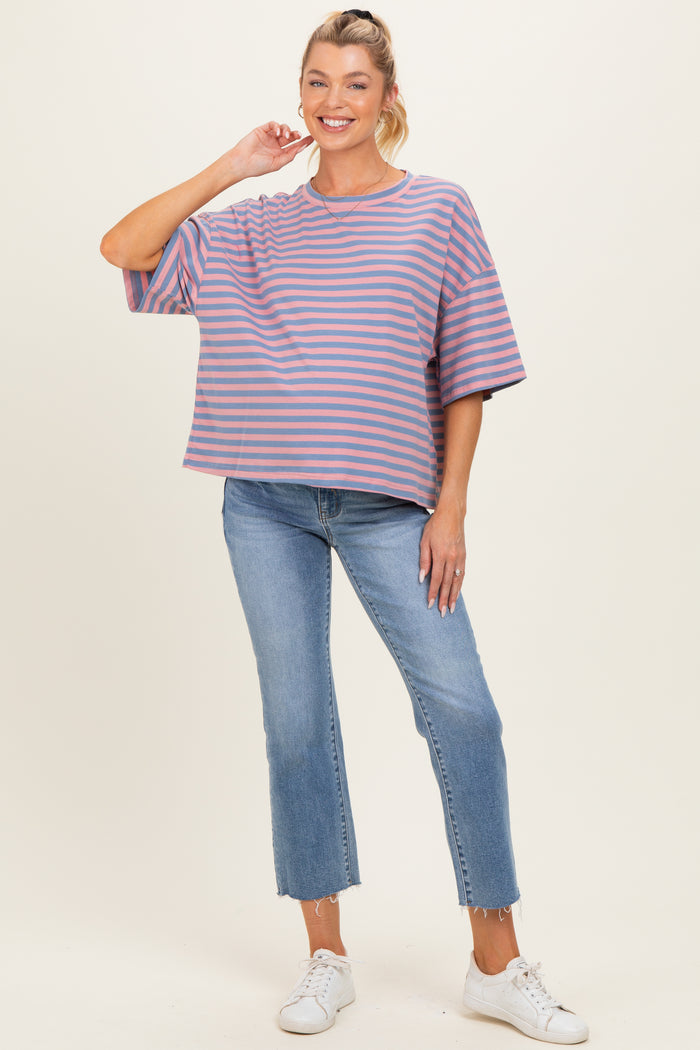 woman wearing a striped purple and pink maternity top with loose fit and blue jeans, smiling and standing with one hand on her hip