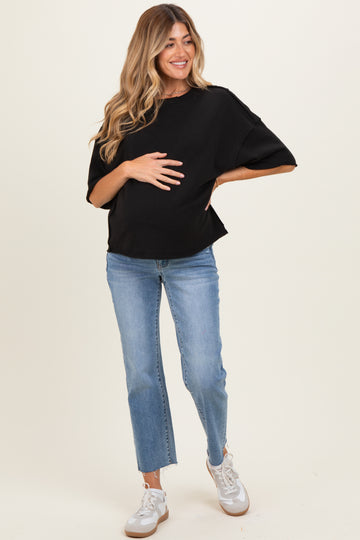 woman wearing a black maternity top and light blue jeans, holding her baby bump with a smile