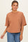 woman wearing a rust orange oversized t-shirt with short sleeves and a raw hem, paired with blue jeans