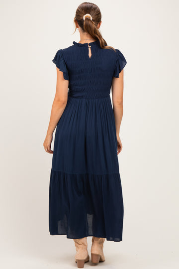 woman wearing a navy blue maternity maxi dress with smocking detail and flutter sleeves, view from the back