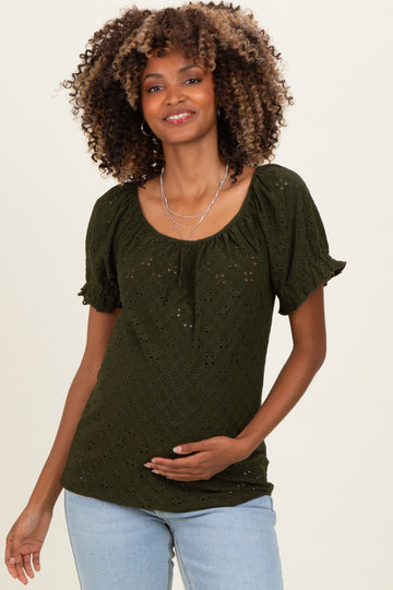 woman wearing a dark green short sleeve maternity top with eyelet details and holding her baby bump