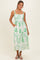 woman wearing a white maxi dress with green leaf print and pockets, styled with a simple necklace and flip flops