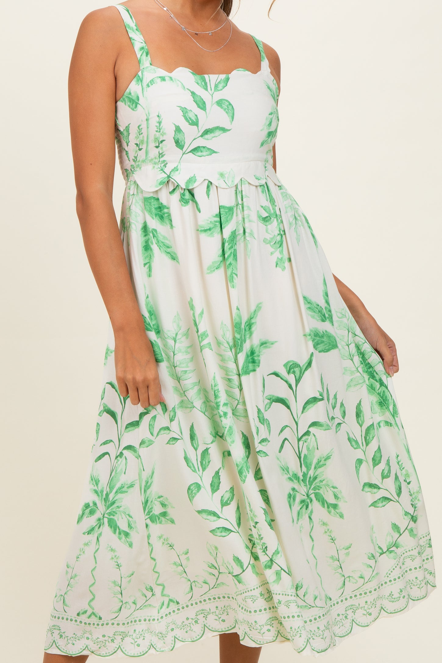 woman wearing a white floral maxi dress with green plant prints and scalloped straps