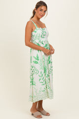 woman wearing a light green floral maxi dress with spaghetti straps and a fitted waist, standing and smiling