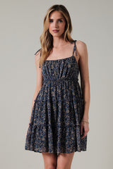 woman wearing a navy blue floral print sundress with tie shoulder straps and tiered ruffles