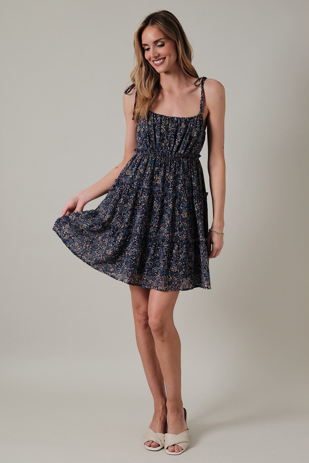 woman wearing a navy floral sundress with adjustable straps and a fitted bodice, smiling and holding the skirt out gently