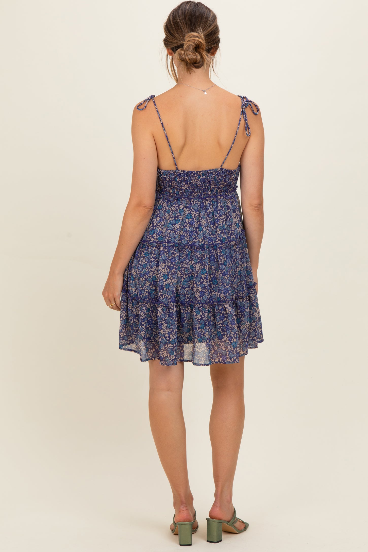 woman wearing a navy floral maternity dress with adjustable tie straps and a tiered skirt, showing a baby bump