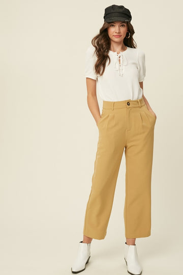 woman wearing a white short sleeve top with lace-up detail and mustard wide-leg trousers