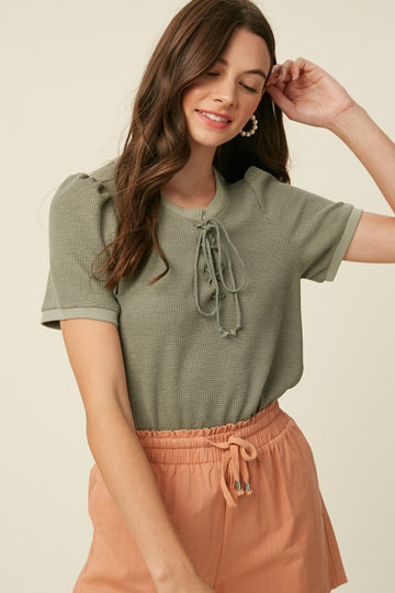 woman wearing a green short sleeve top with lace-up front and peach drawstring shorts