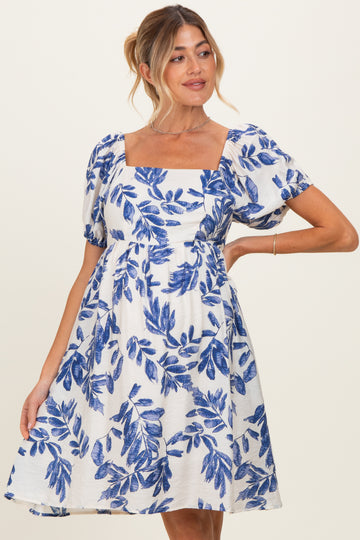 woman wearing a white maternity dress with blue floral print and puff sleeves, gently hugging her baby bump