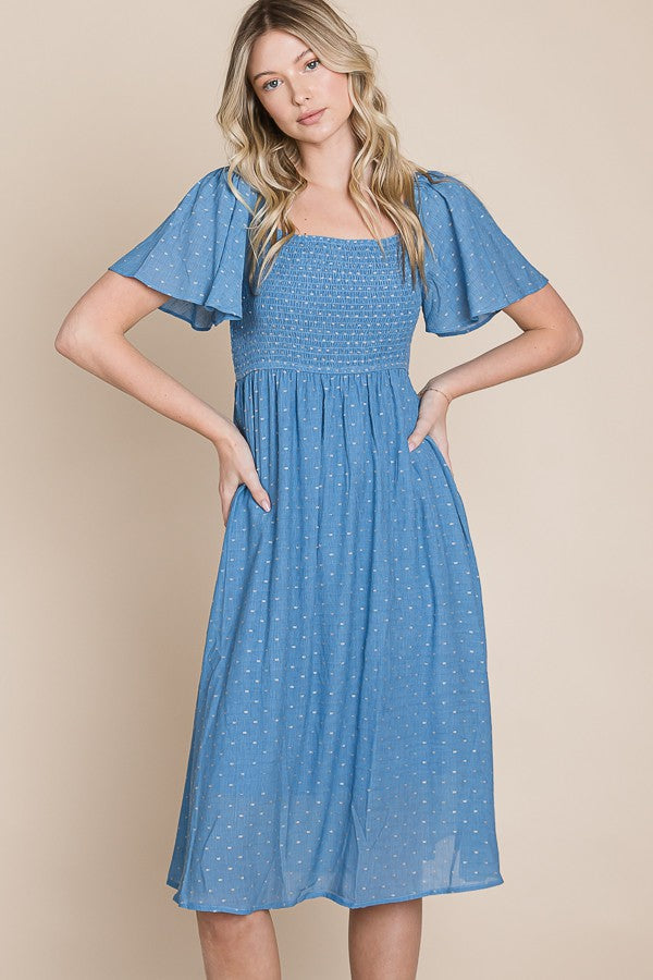 woman wearing a light blue midi dress with flutter sleeves and smocked bodice, standing against a neutral background