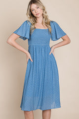 woman wearing a light blue midi dress with flutter sleeves and smocked bodice, standing against a neutral background