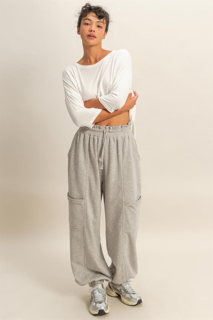 woman wearing a white long sleeve top and gray wide-leg sweatpants with pockets