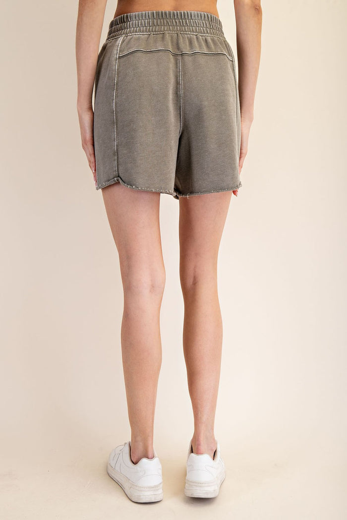 woman wearing olive green denim shorts with a frayed hem and elastic waistband, viewed from the back