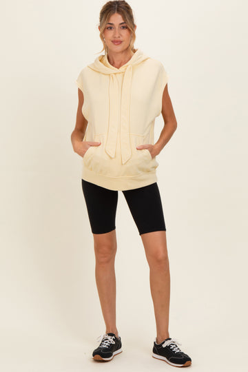 woman wearing a light yellow sleeveless maternity hoodie with pockets and black bike shorts