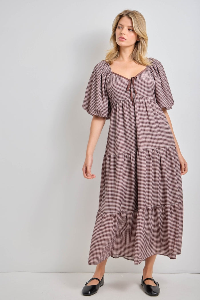 woman wearing a brown and white checkered maxi dress with puff sleeves and a tie detail at the neckline
