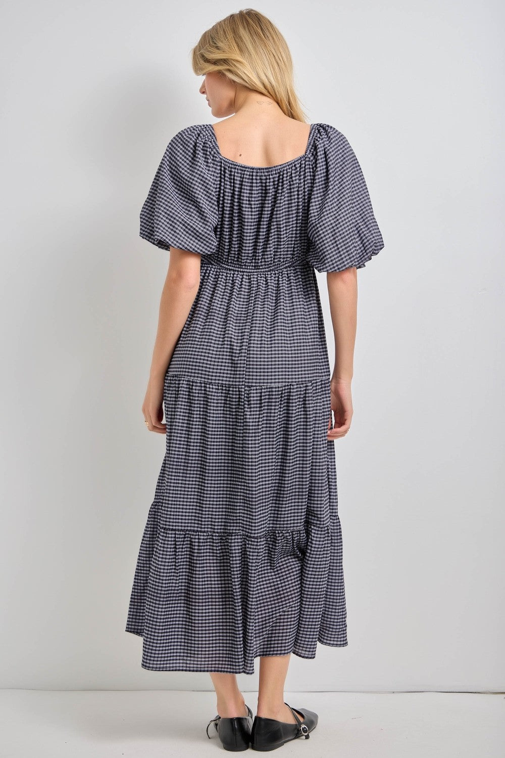 woman wearing a navy and white checked maxi dress with puff sleeves and tiered skirt, shown from the back