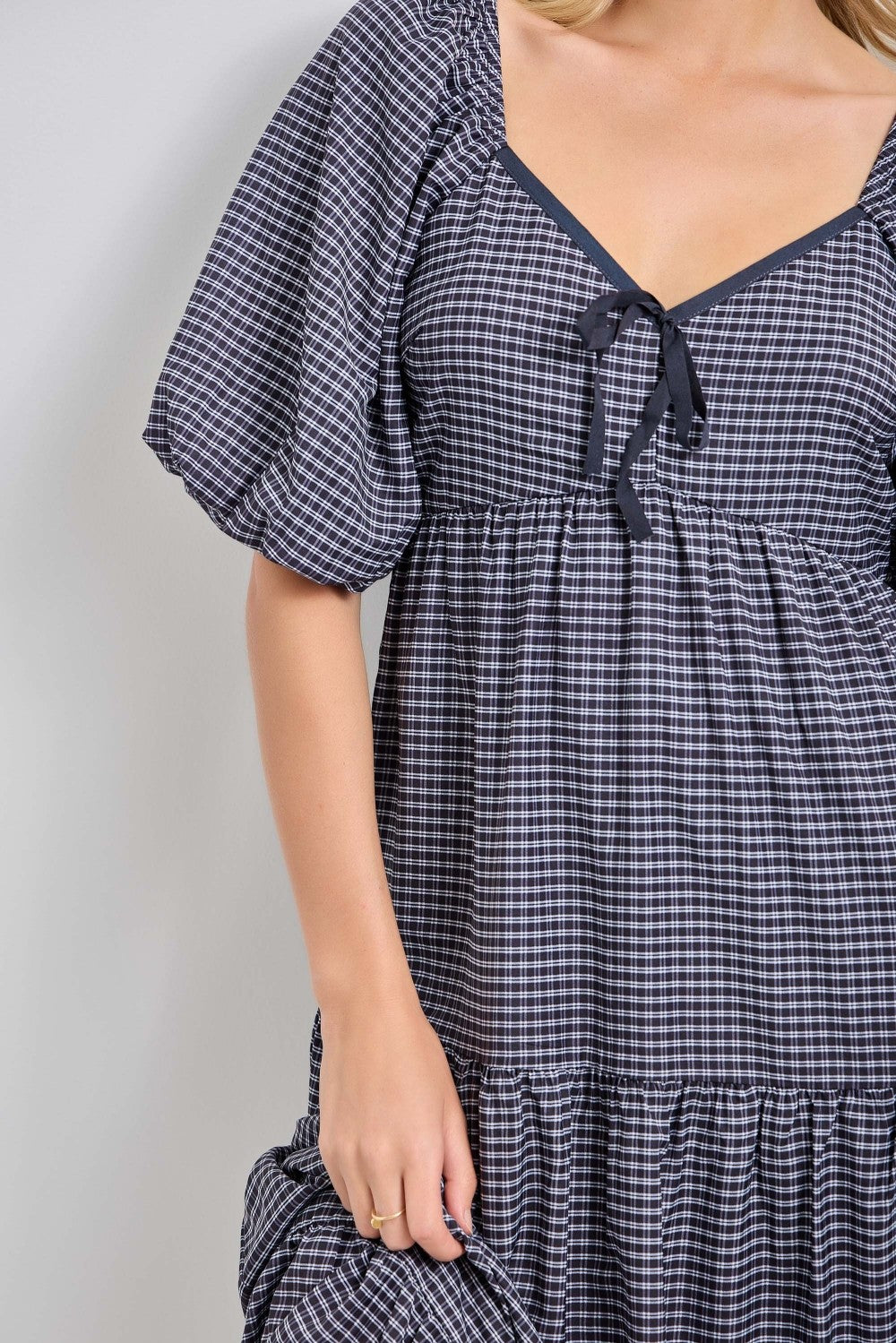 woman wearing a black and white checked puff sleeve dress with a tie detail at the neckline